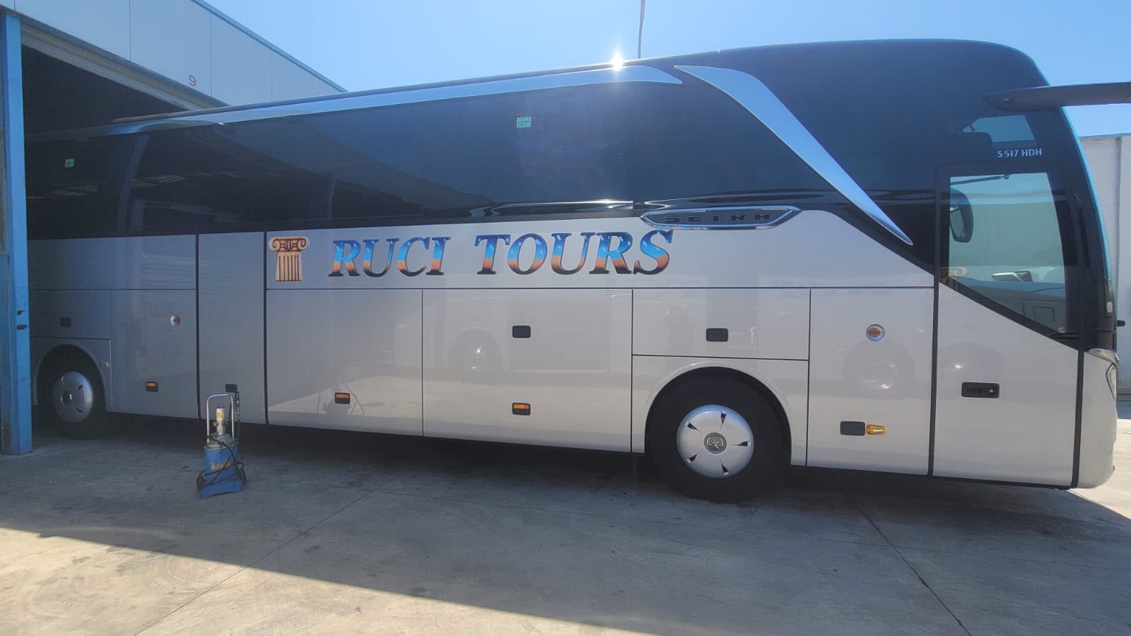 Autobus Setra ngjyrë argjendi me shkronja RUCI TOURS blu-ari dhe logo kolone antike, në diell