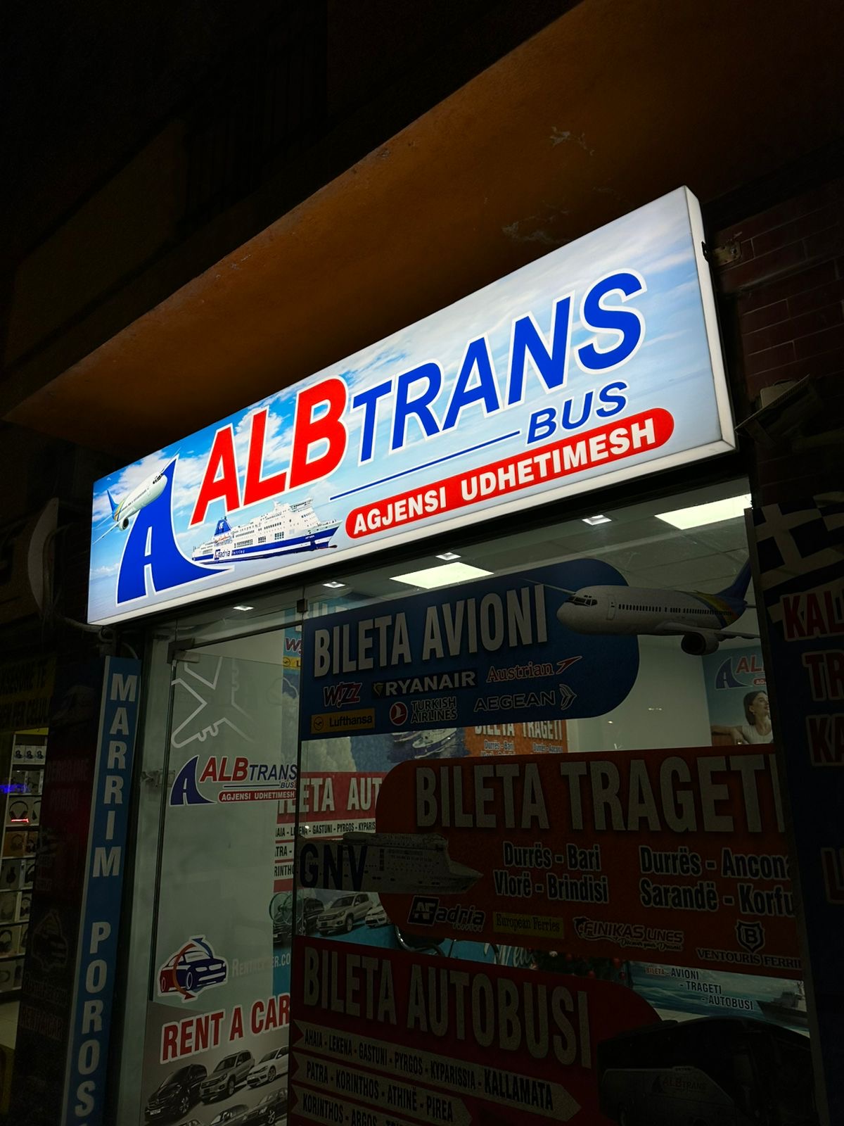 Lightbox i ndriçuar i agjencisë AlbTrans Bus natën, me grafika bilete në vitrinë