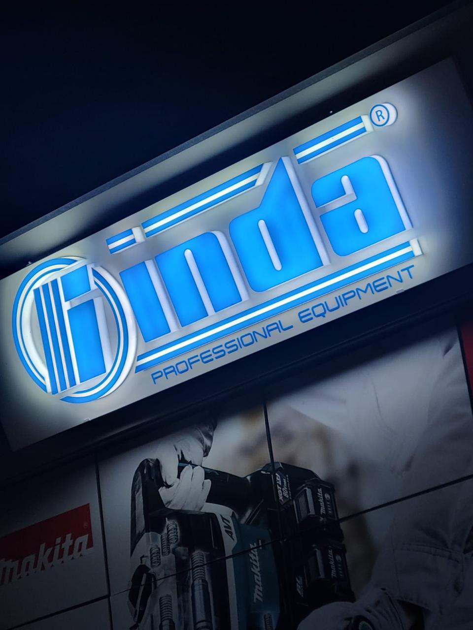 Logo inda me shkronja blu të ndriçuara dhe grafikë Makita në fasadën e dyqanit të veglave natën