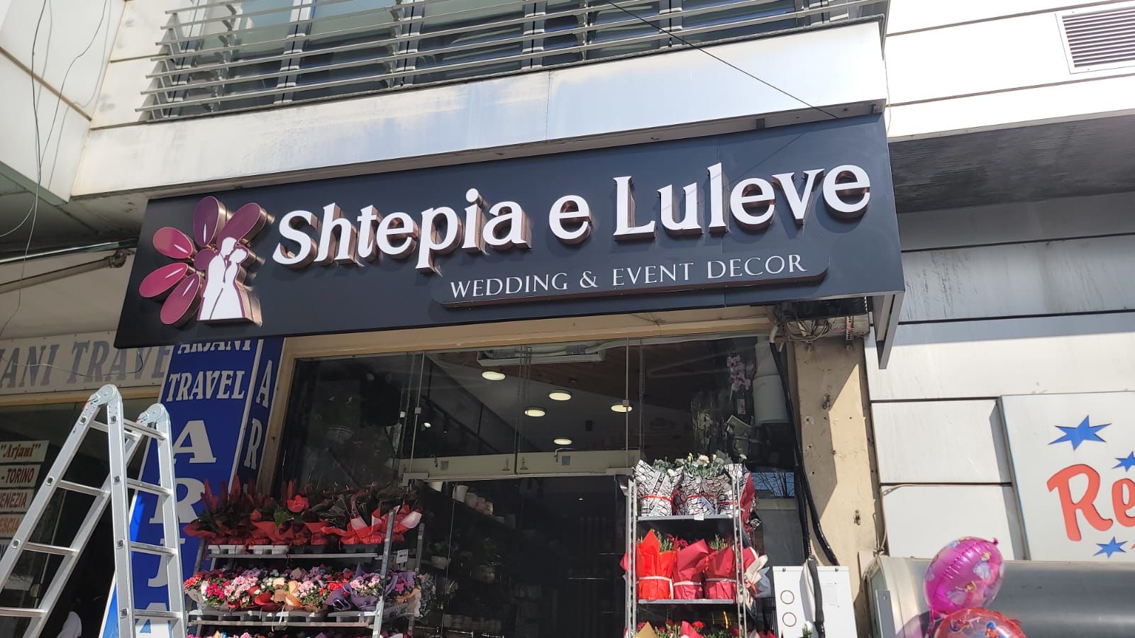 Shkronja 3D të bardha dhe logo lulesh magenta mbi hyrjen e dyqanit të luleve