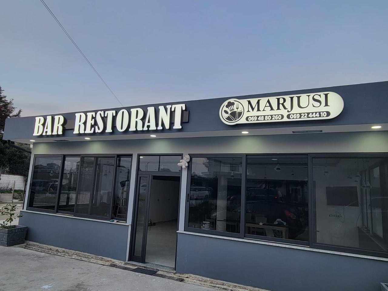 Shkronja të ndriçuara BAR RESTORANT dhe lightbox oval Marjusi me numra telefoni, të ndezura në muzg